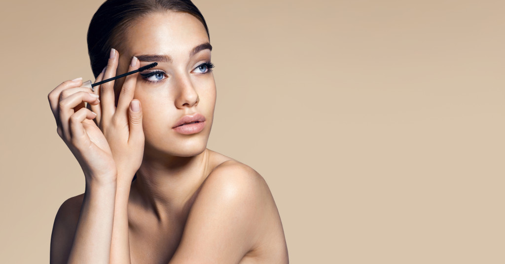 Mascara applying. Makeup closeup. Eyes make-up / photos of appealing brunette girl on beige background