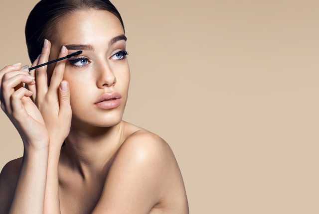 Mascara applying. Makeup closeup. Eyes make-up / photos of appealing brunette girl on beige background